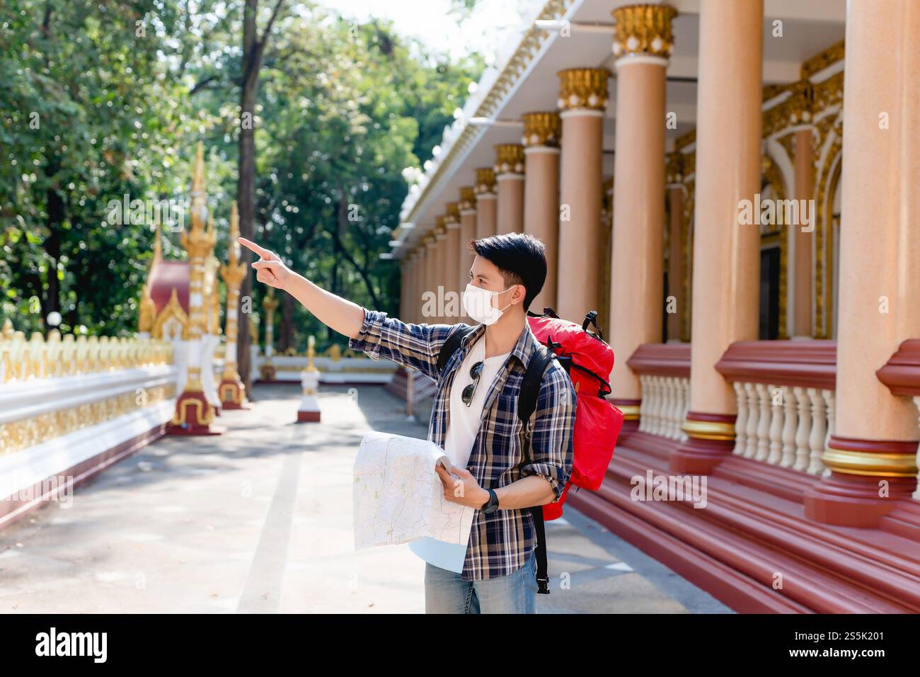 Portrait Young Asian backpacker male in face mask standing and checking ...