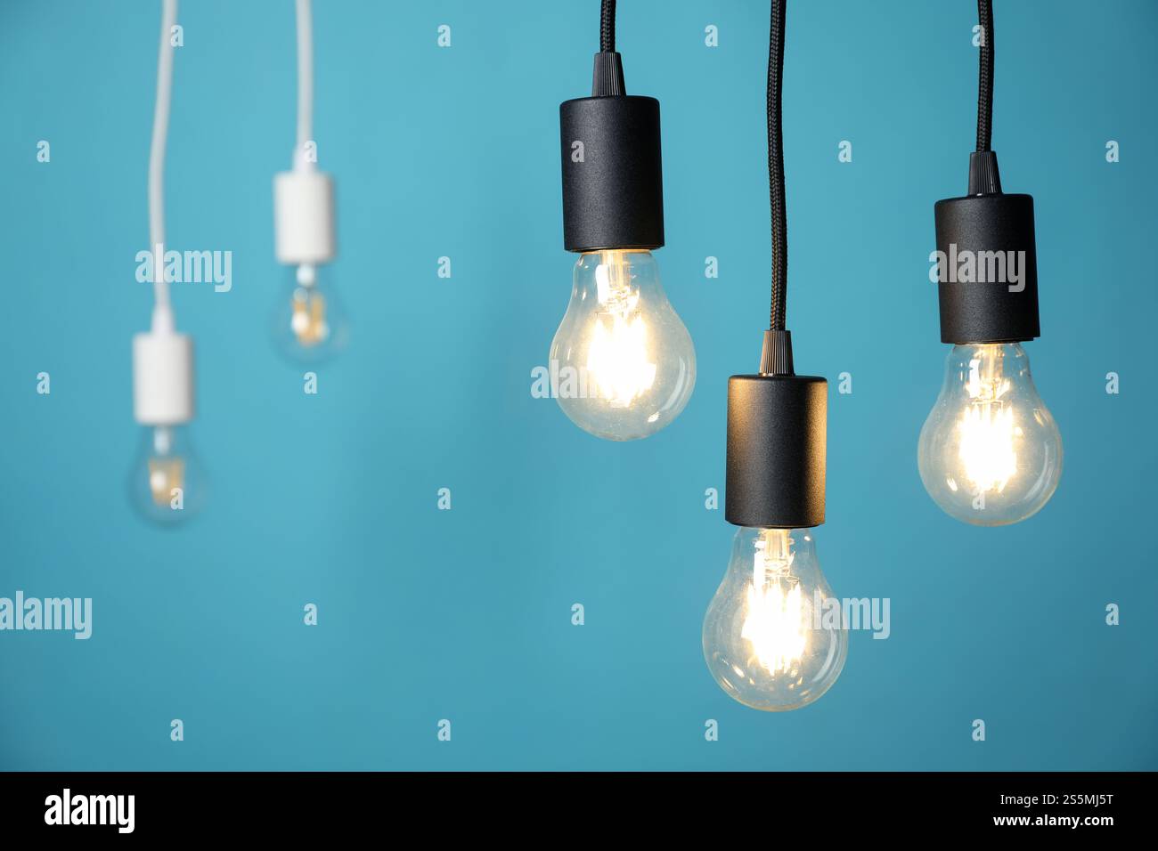 Light bulbs hanging on cords against blue background, selective focus Stock Photo