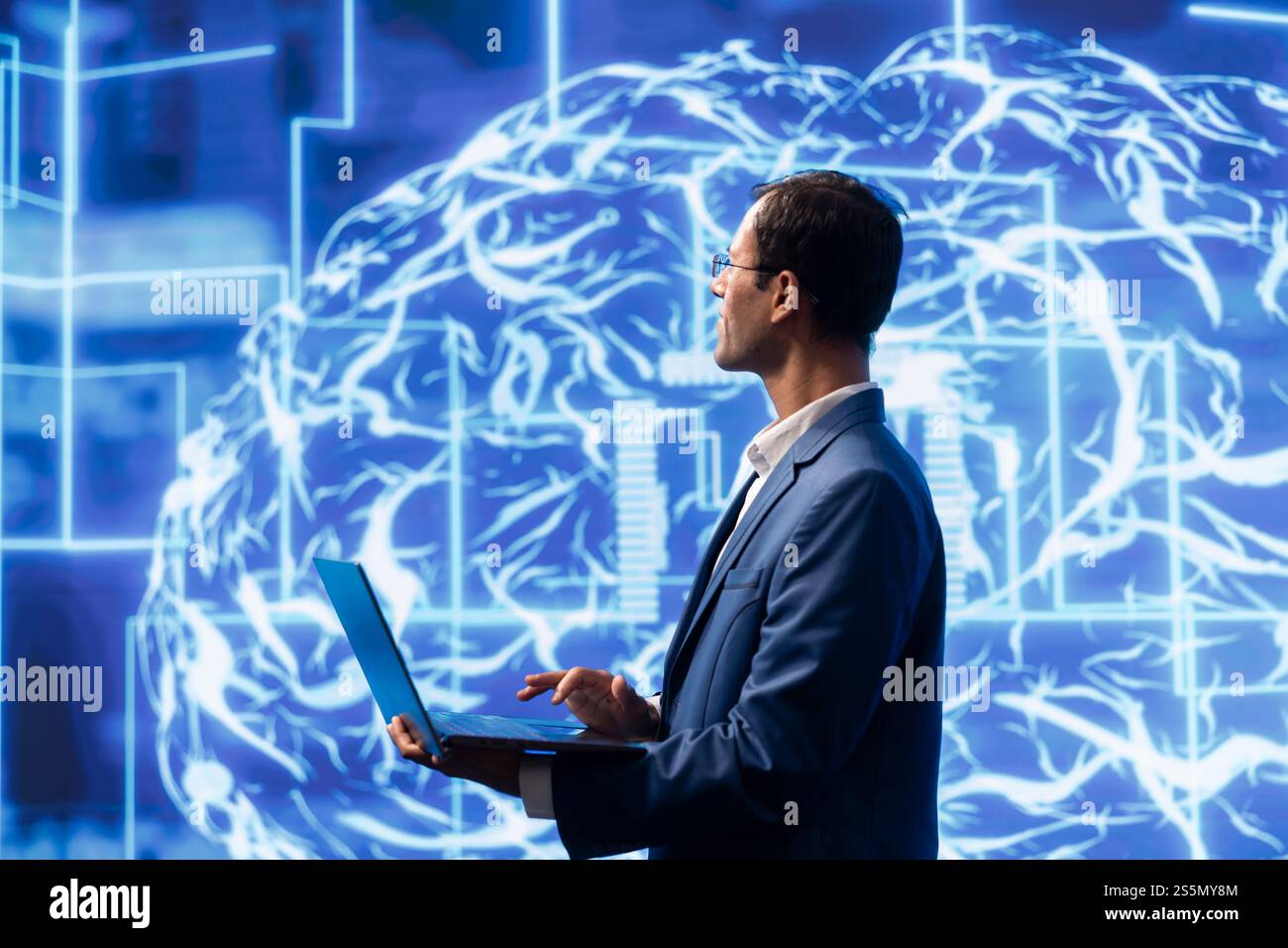 Computer scientist analyzes AI models with large digital brain displayed behind. IT specialist in workspace using machine learning to better understand and develop artificial intelligence Stock Photo