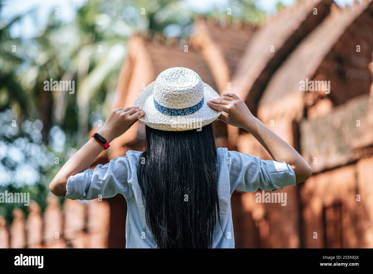 Back view, Young woman with long black hair wearing hat, blurred background with ancient site, copy space Stock Photo