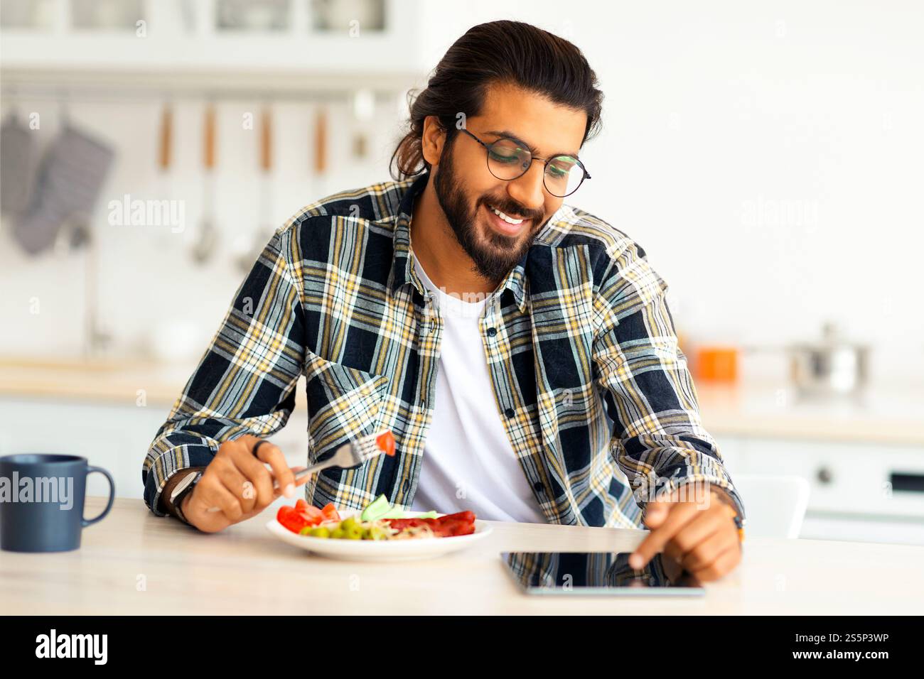 Positive arab guy having breakfast, using digital tablet, copy space Stock Photo
