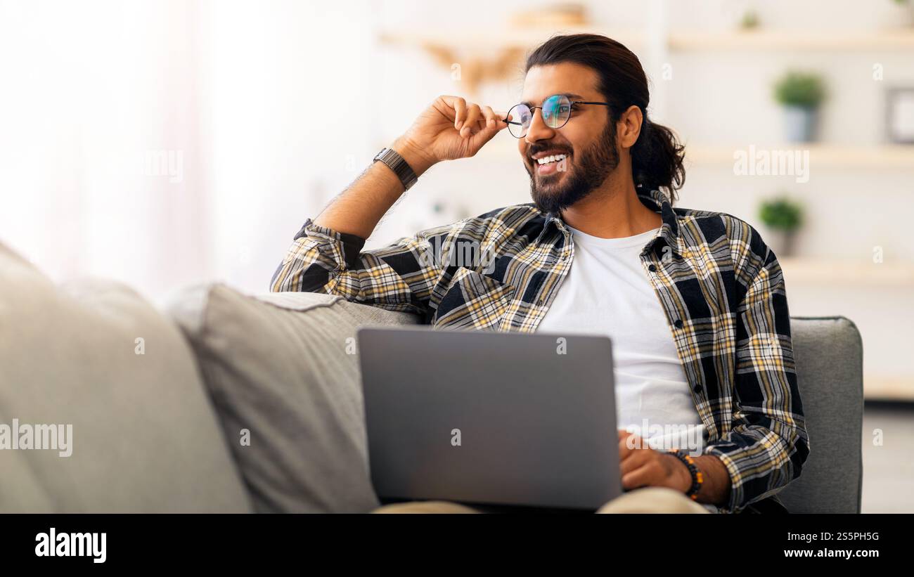 Dreamy arab guy freelancer working from home, using laptop Stock Photo