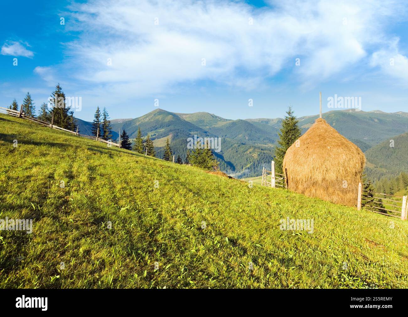 Summer mountain village outskirts with field and haystack Stock Photo