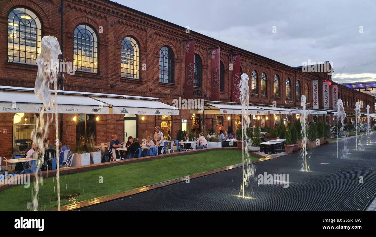 People sitting in a cafe along a red brick facade. Fountain in the foreground, Manufaktura, lodZ, Lodz, Lodz, Poland, Europe Stock Photo