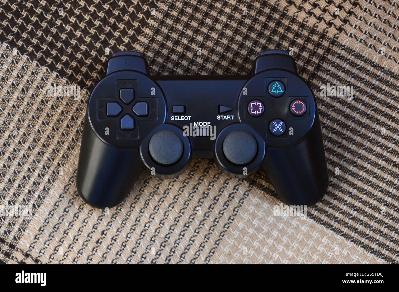 The video game controller from the game console is on the checkered sofa. Wireless device for controlling during video games. Video game controller Stock Photo