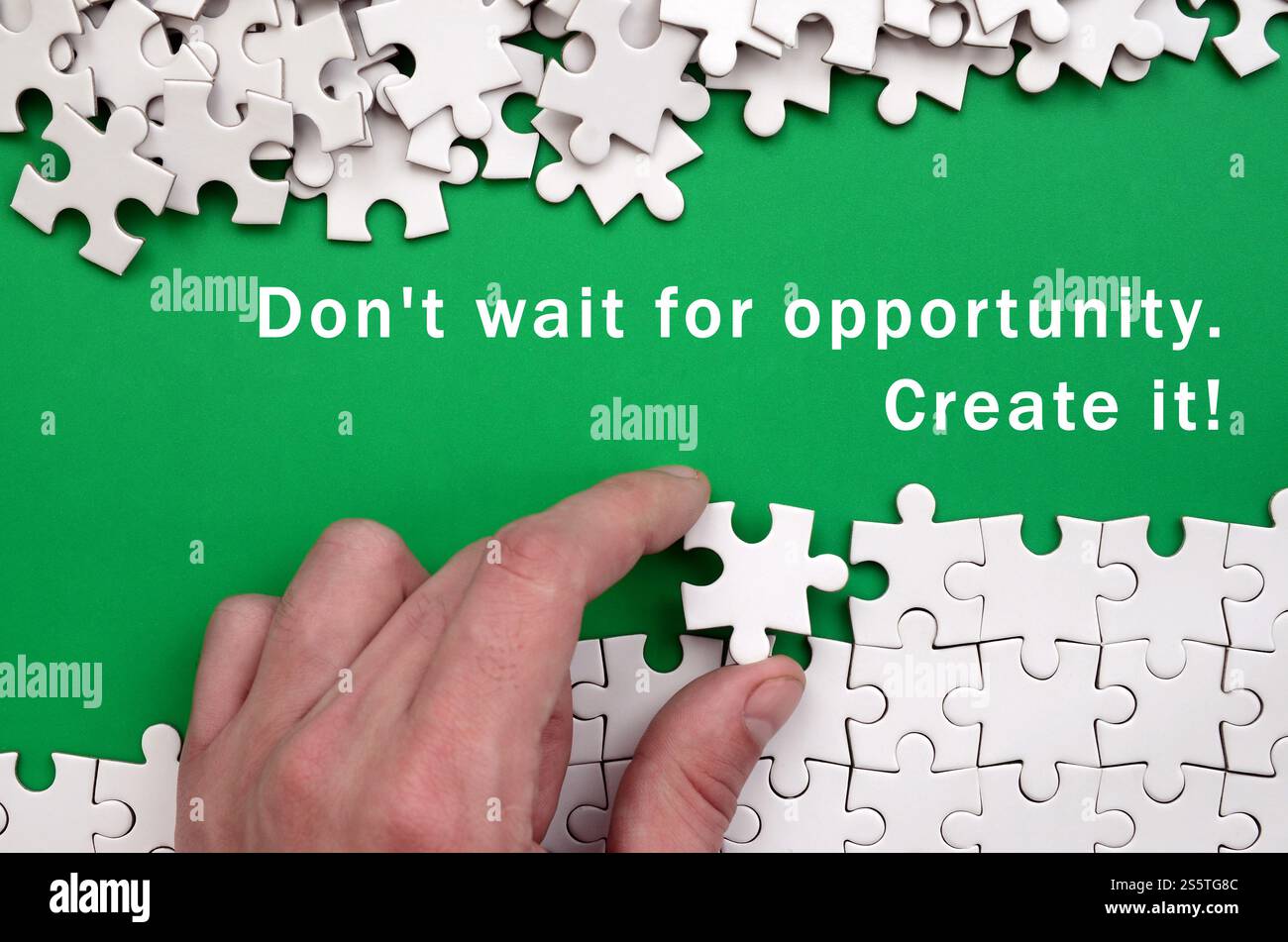 Dont wait for opportunity. Create it. The hand folds a white jigsaw puzzle and a pile of uncombed puzzle pieces lies against the background of the Stock Photo