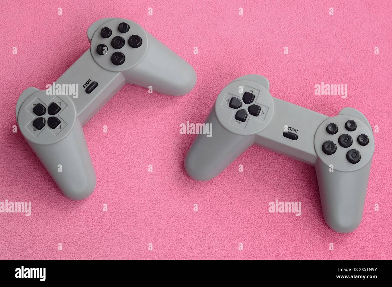Playing games concept. Two pad joysticks lies on the blanket of furry pink fleece fabric. Controllers for video games on a background texture of Stock Photo