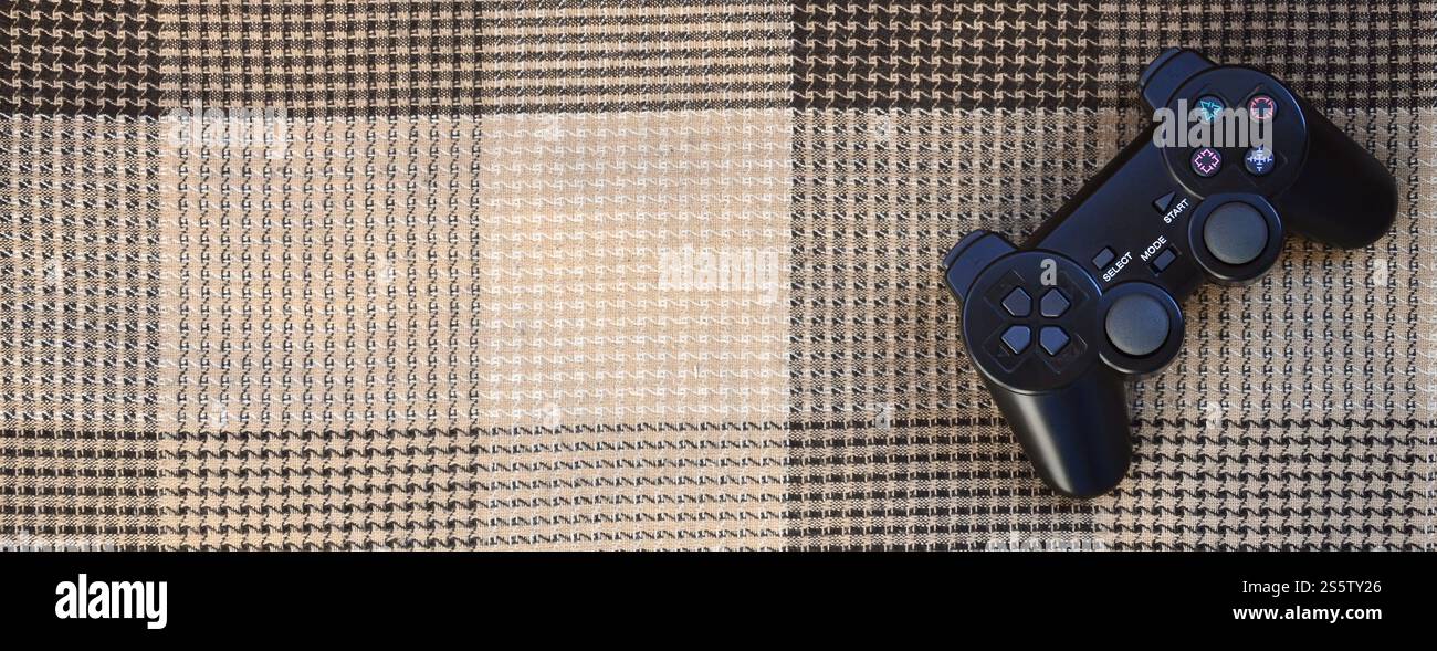 The video game controller from the game console is on the checkered sofa. Wireless device for controlling during video games. Video game controller Stock Photo
