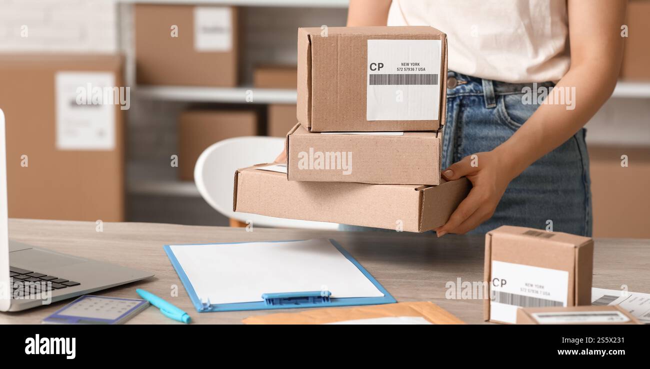 Female postal worker putting parcel boxes on table in warehouse Stock Photo