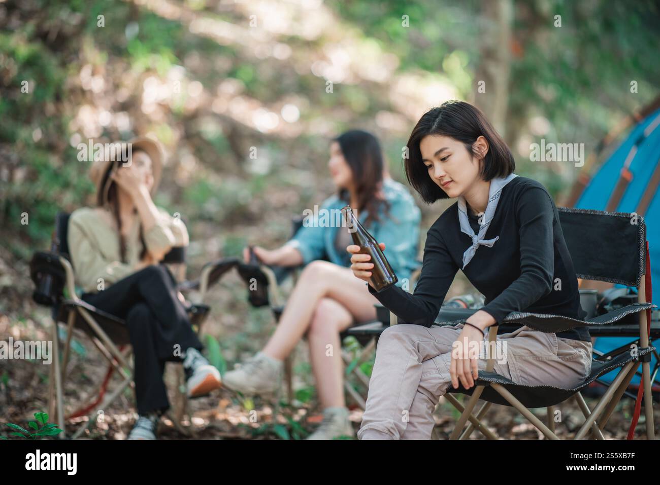 Selective focuse, beautiful Asian woman and friends travelers relaxing at front of camping tent, They enjoy to talking and drinking beer with fun and Stock Photo