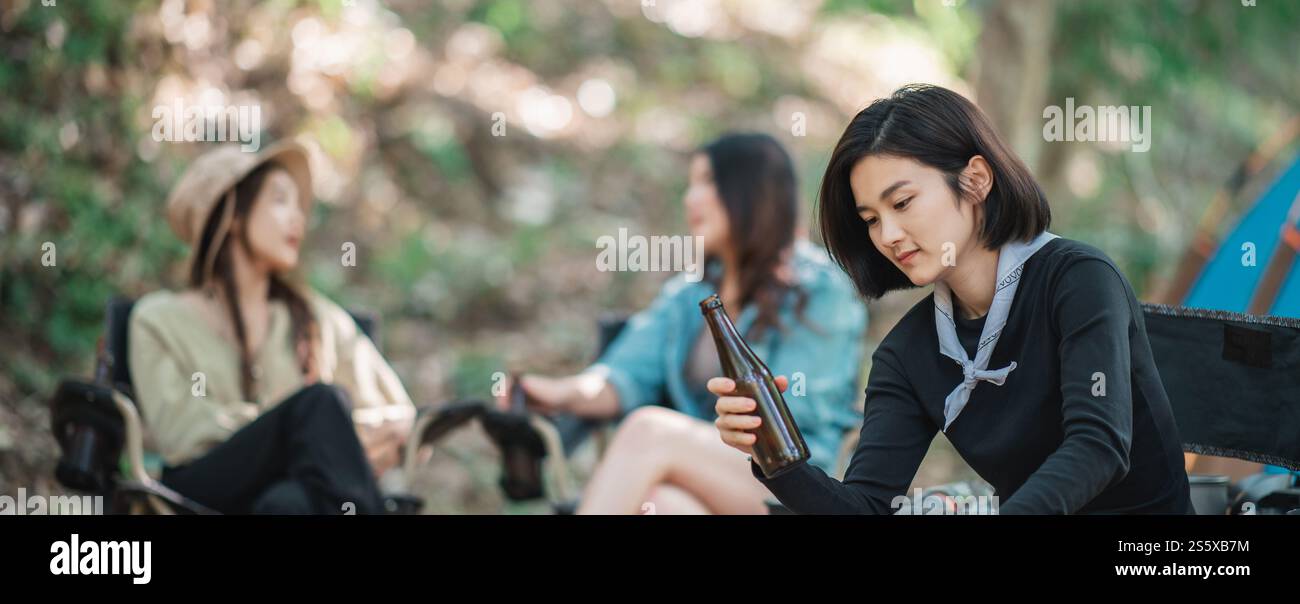 Selective focuse, beautiful Asian woman and friends travelers relaxing at front of camping tent, They enjoy to talking and drinking beer with fun and Stock Photo