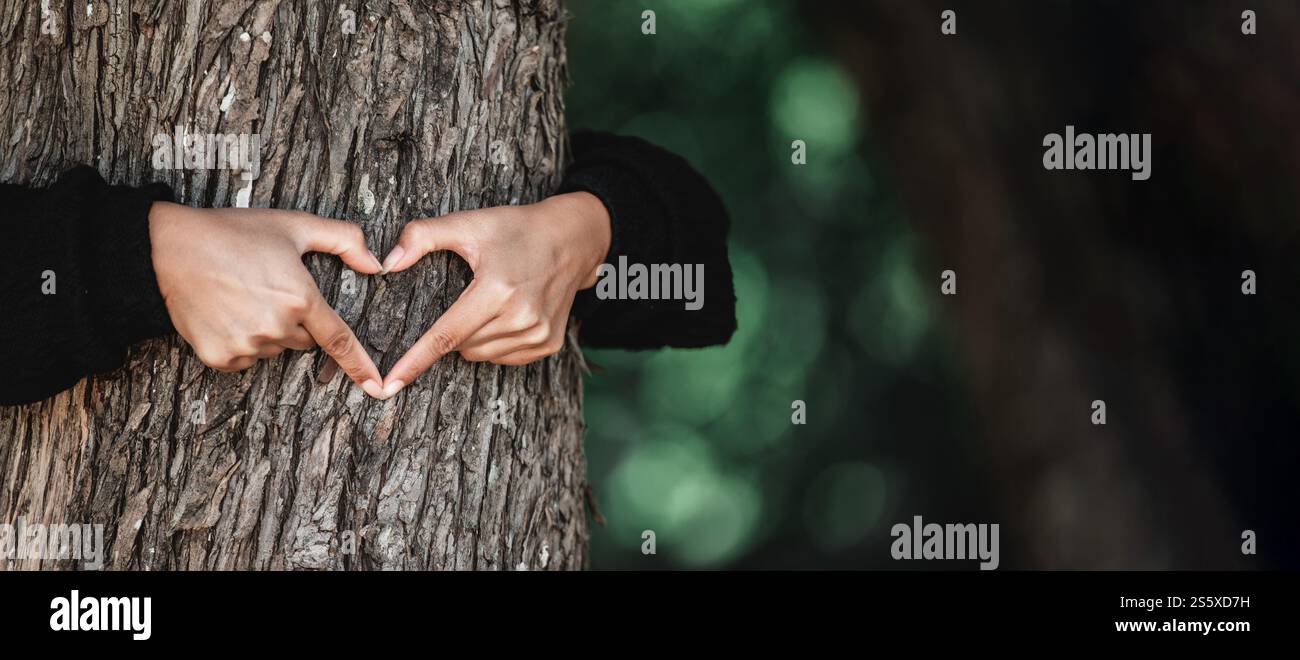 Young woman hug a tree in the forest and show a sign of heart and love ...