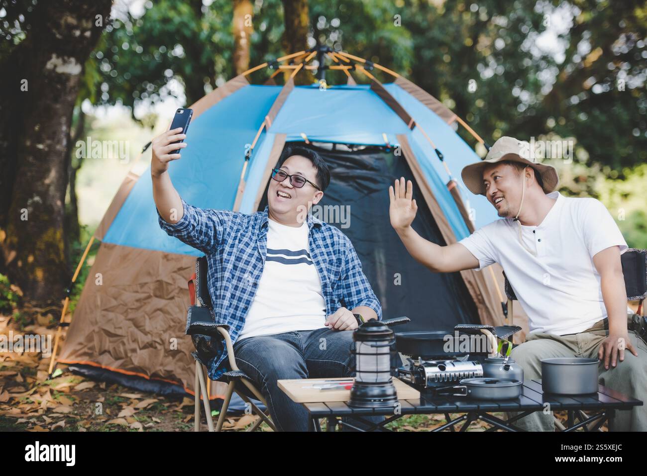 Portrait happy Asian man friends Making a video call with smartphone in camping. Cooking set front ground. Outdoor cooking, traveling, camping, Stock Photo