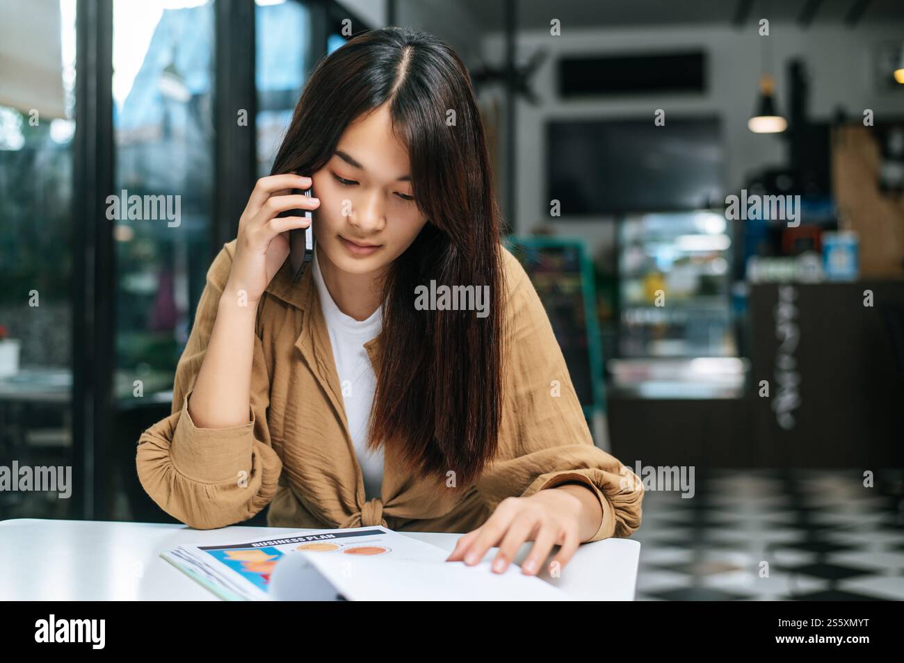 Close up, Young woman use smartphone while working on laptop and paperwork or report presenting Project growth graph at cafe Stock Photo