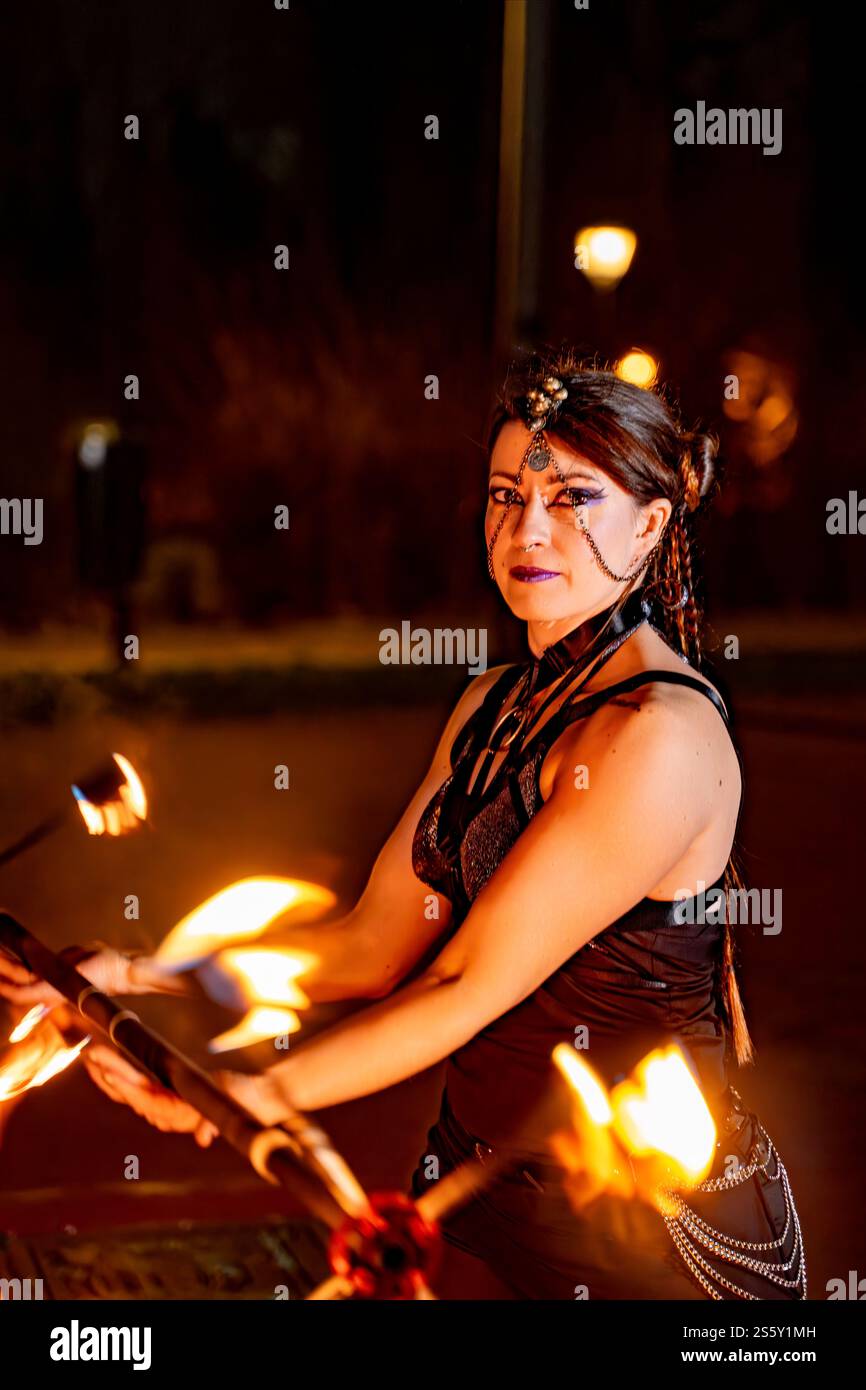 Female fire performer twirling a flaming staff at night, generating mesmerizing light trails against a dark backdrop, showcasing skill and passion Stock Photo