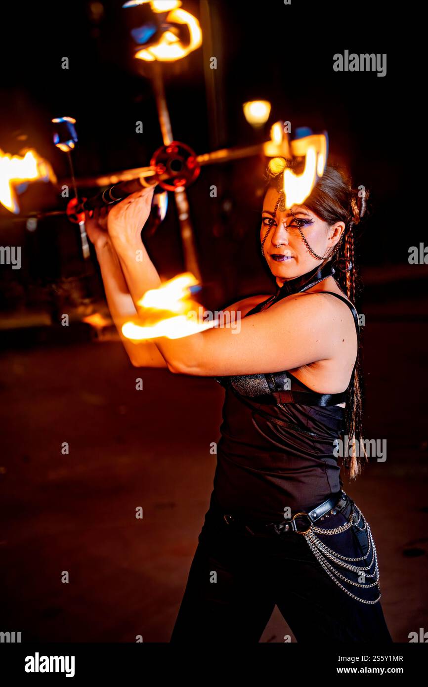 Female artist captivating an audience with a mesmerizing fire dance performance, skillfully juggling burning torches against the night sky Stock Photo