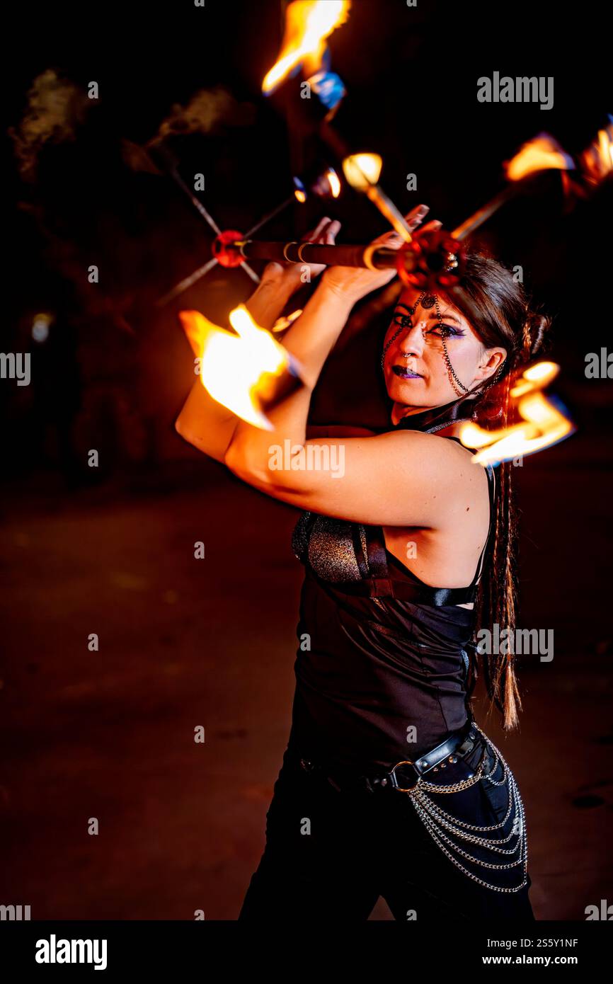 Female fire artist performing with multiple torches, creating a mesmerizing spectacle with flames against a dark backdrop Stock Photo