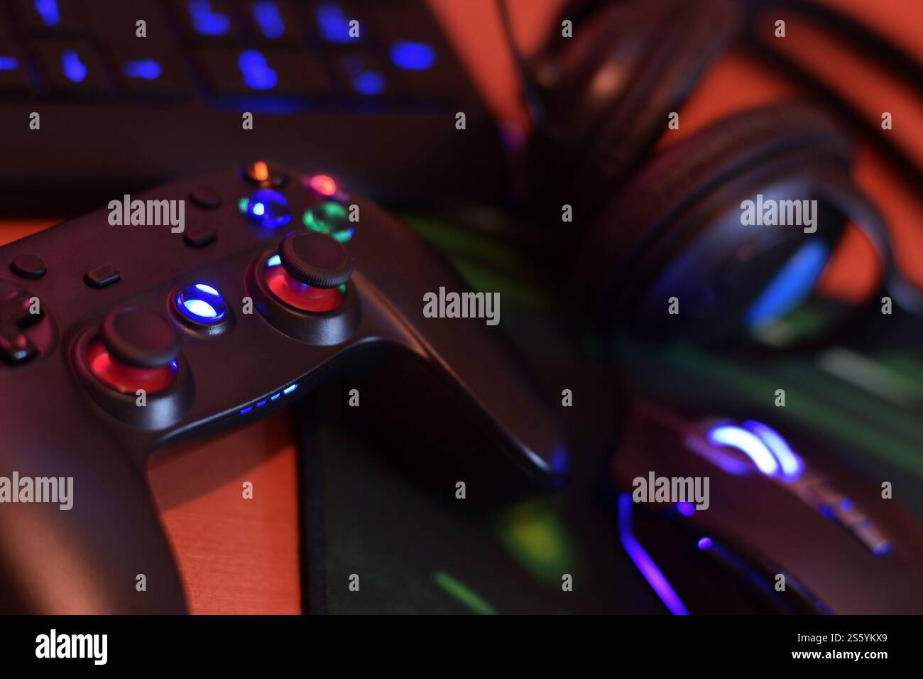 Modern gamepad and gaming mouse lies with keyboard and headphones on table in dark playroom scene close up. Modern electronics for professional Stock Photo