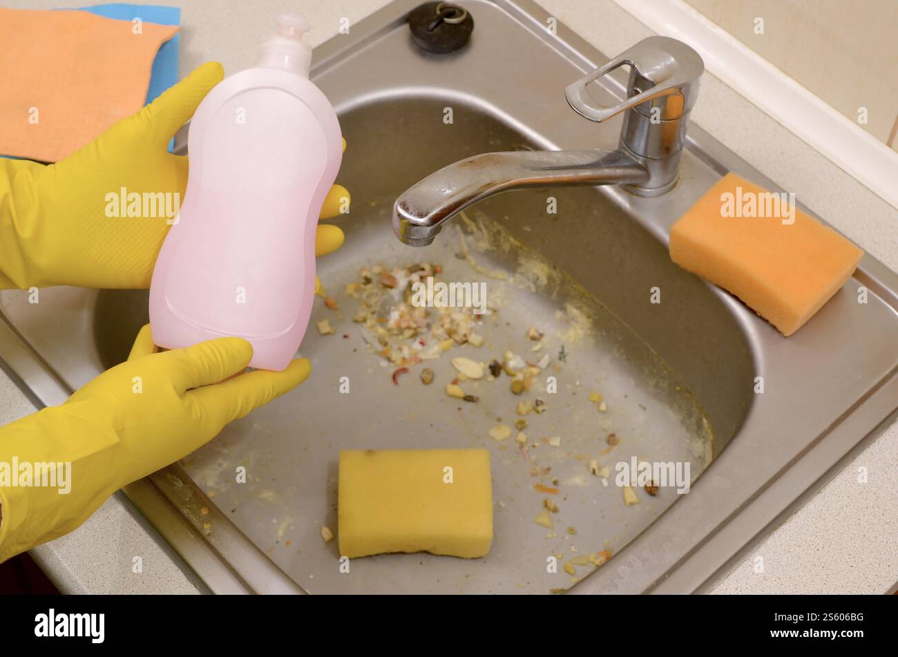 People housework washing-up and housekeeping concept. Cleaner shows liquid cleanser detergent bottle at dirty kitchen sink with food particles before Stock Photo