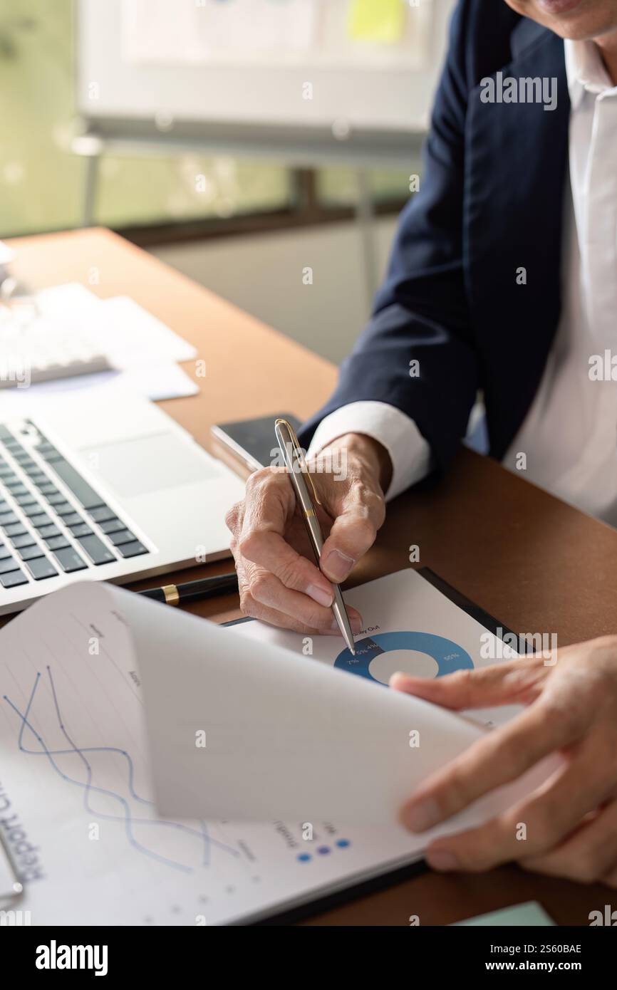 Elderly businessman analyzing data and taking notes in a modern office setting Stock Photo