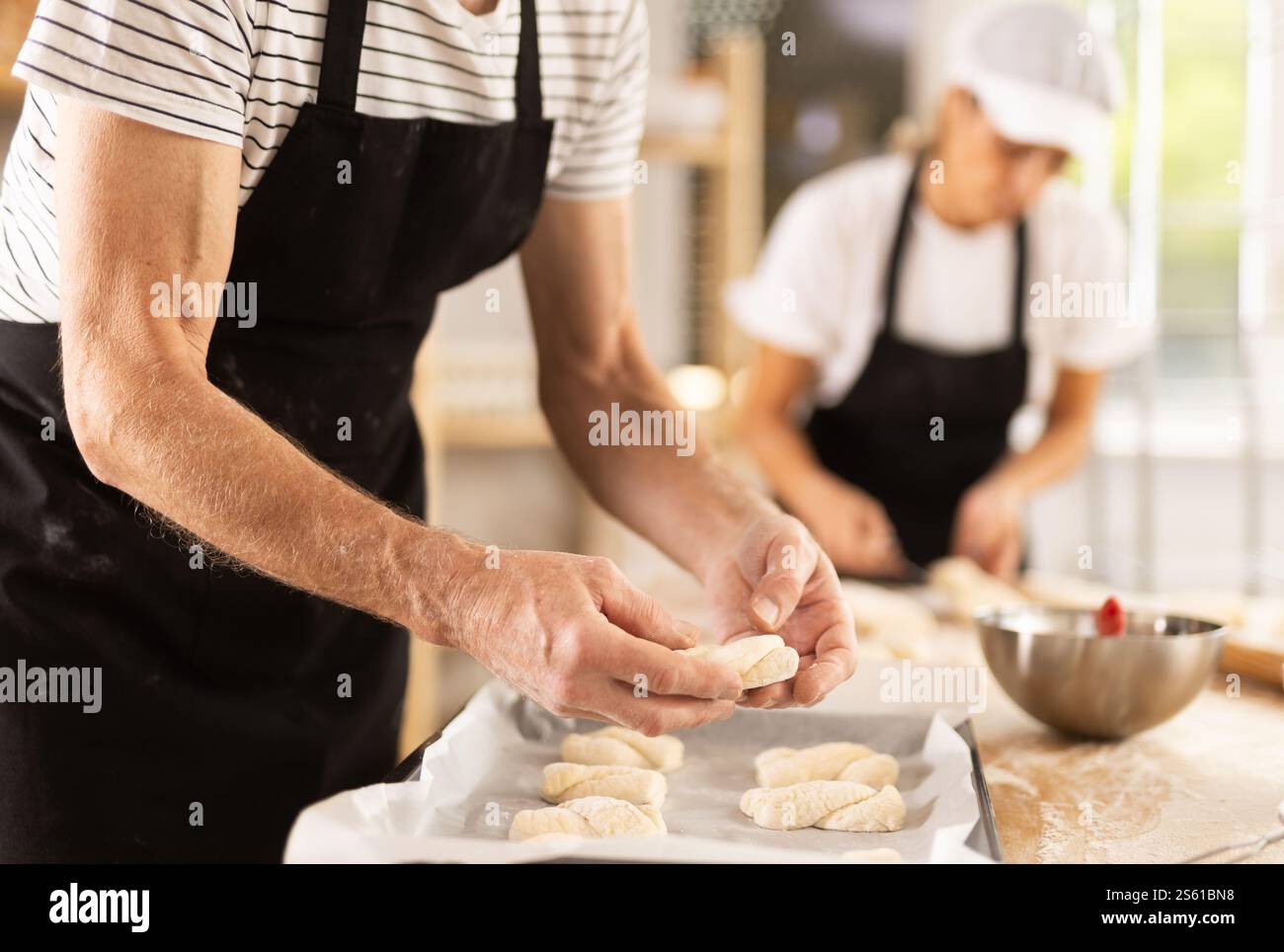 Baker's hands fold pieces of dough on baking sheet Stock Photo