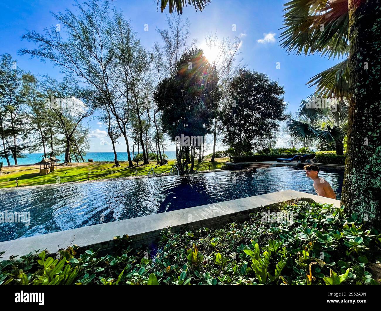 View over pool towards the sea, blue sky, smaal clouds and trees - Smartphone Captured Stock Image