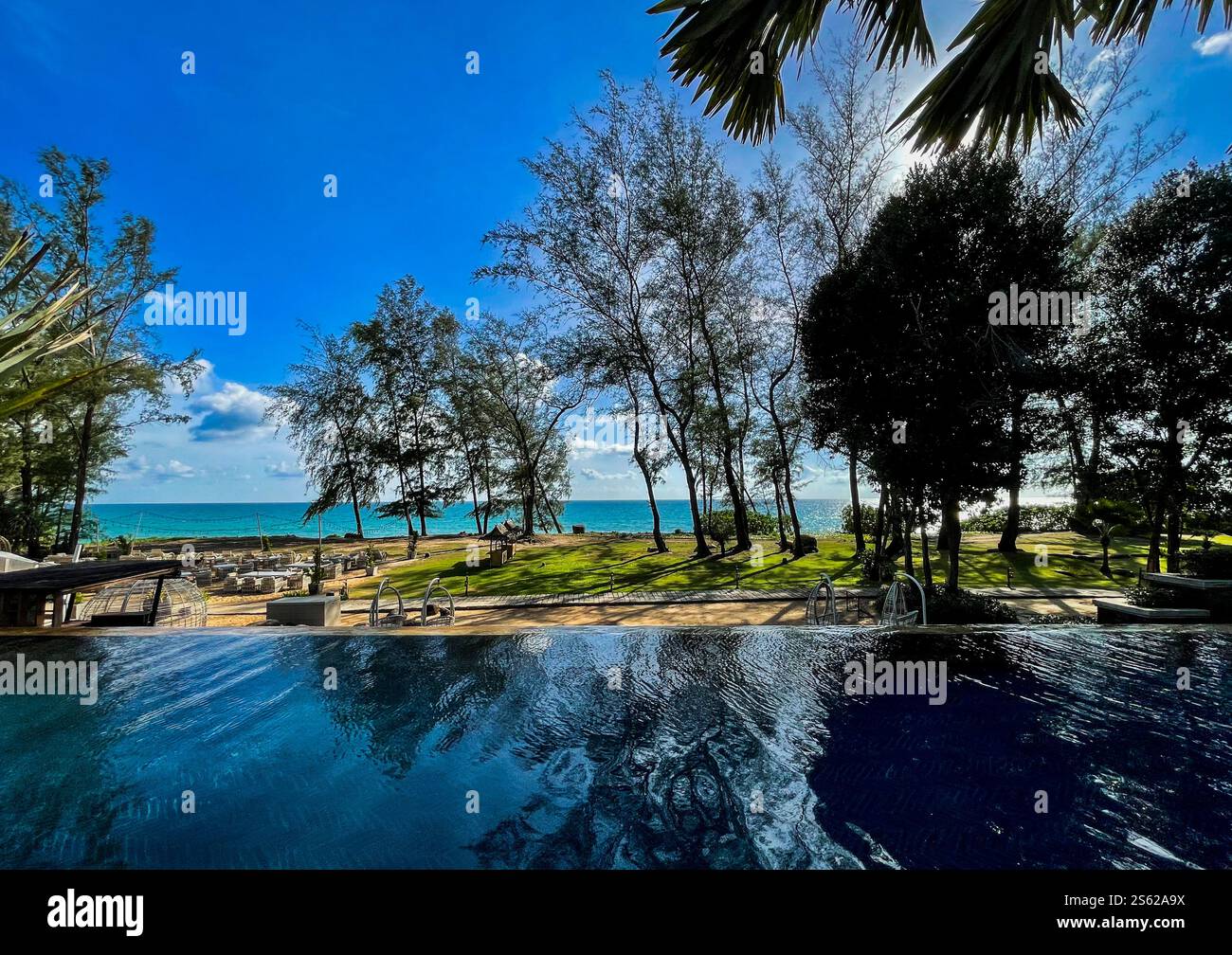 View over pool towards the sea with blue sky, small clouds and trees - Smartphone Captured Stock Image