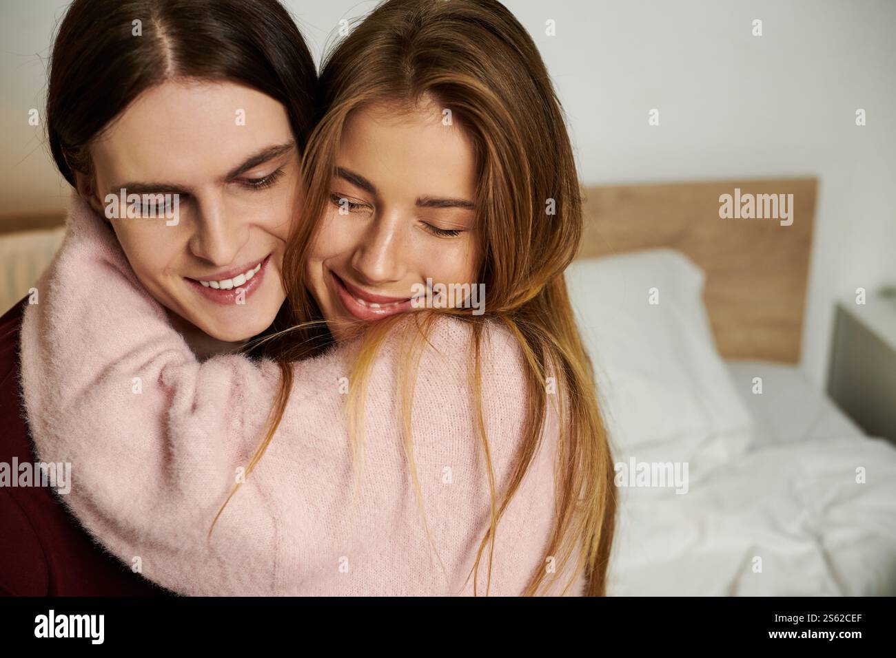 A young couple shares a warm embrace, smiling joyfully in a stylish bedroom filled with light. Stock Photo