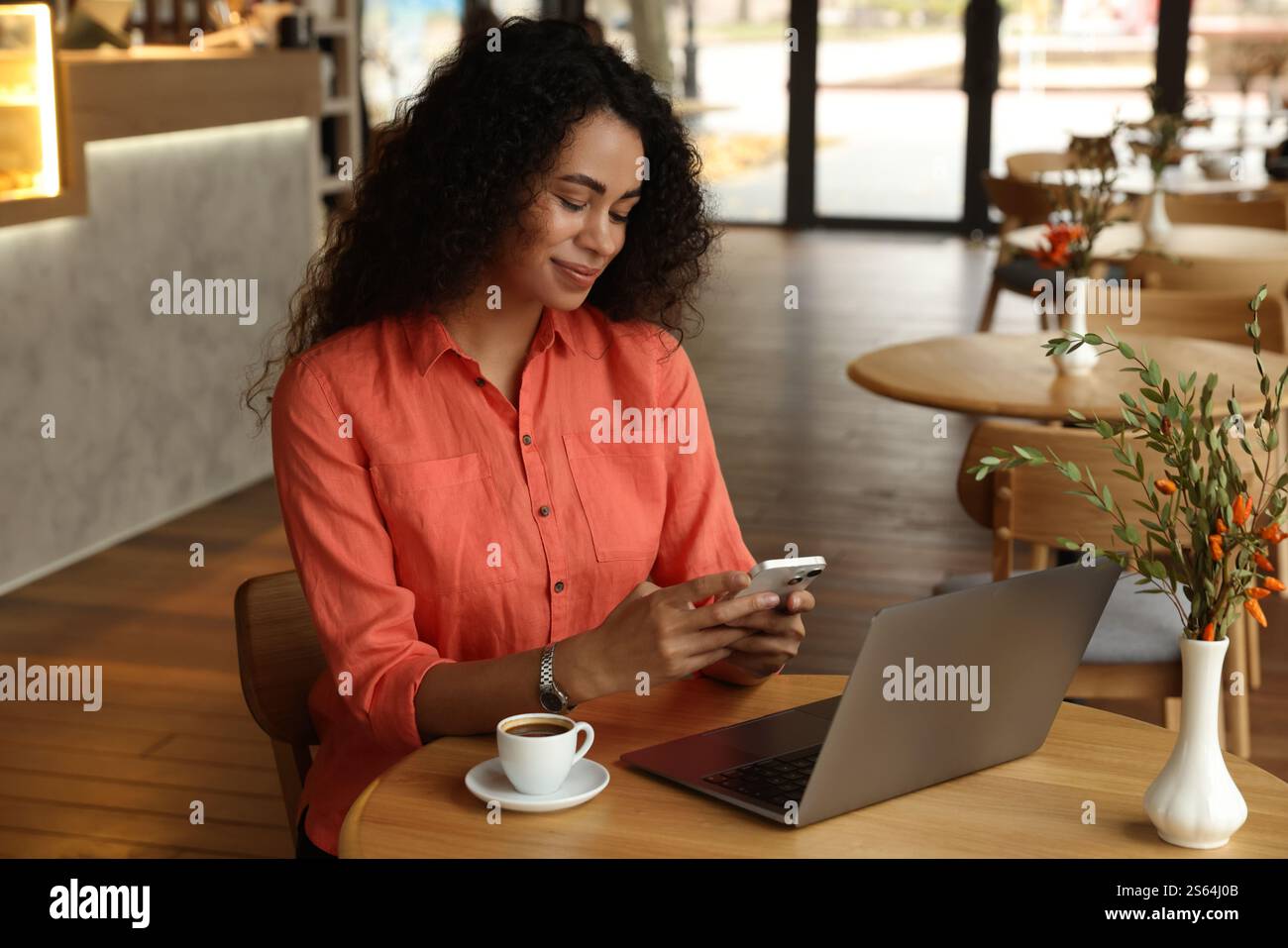 Woman using smartphone while working in cafe Stock Photo