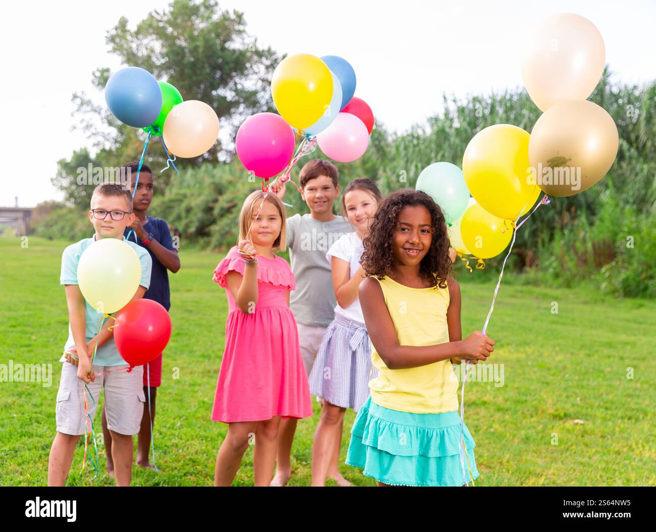 Smiling african american preteen girl with balloons on green lawn with ...
