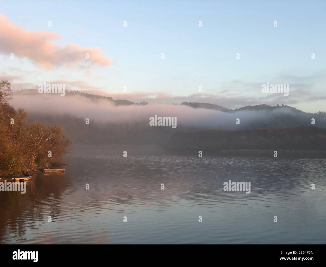 Silhouette of a woman standing on a River bank looking at a sun setting on the horizon. - Smartphone Captured Stock Image