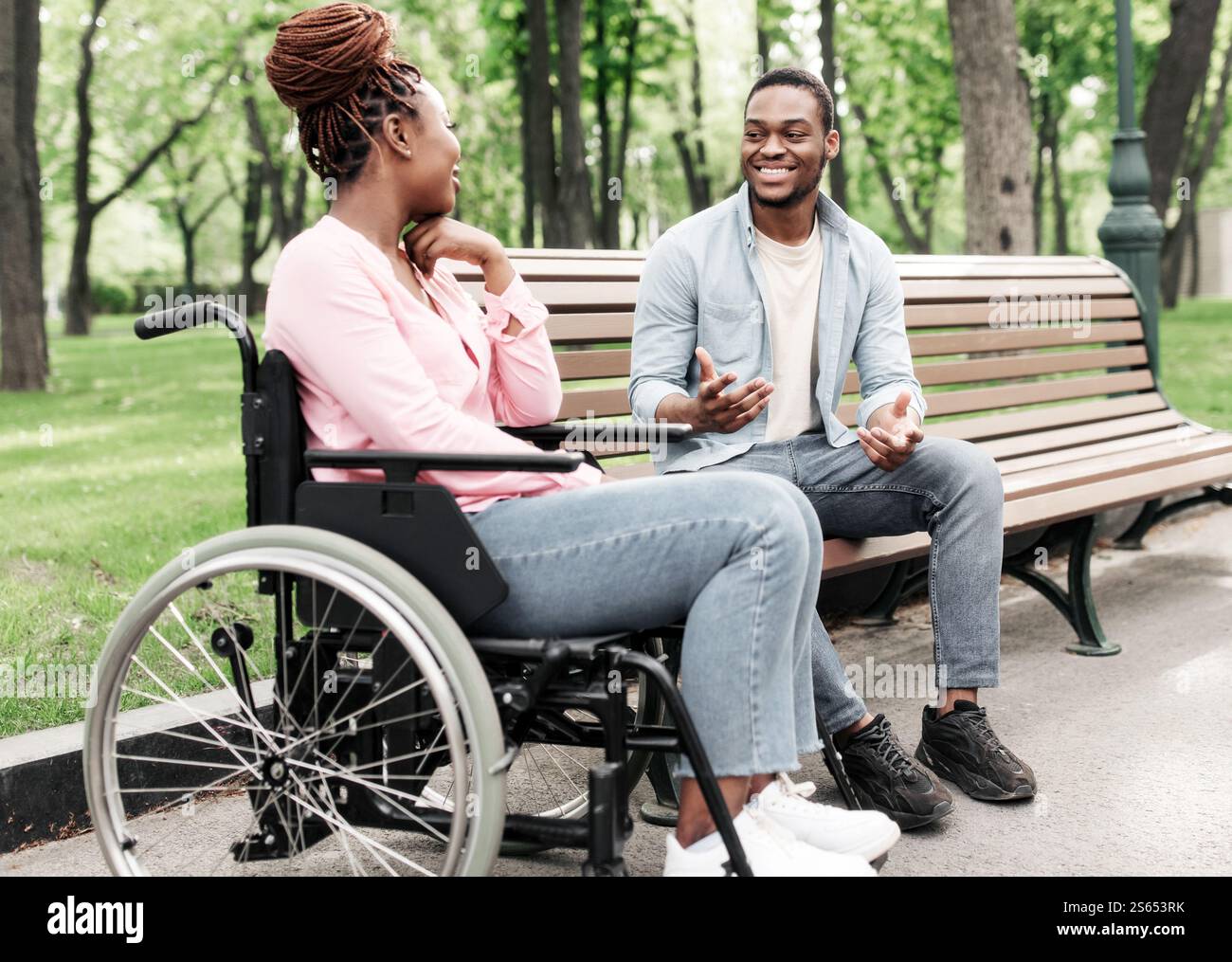 Happy young black woman in wheelchair talking to her boyfriend at park ...