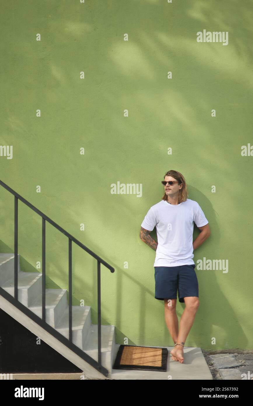 A man casually leaning against a vibrant green wall beside a set of ...