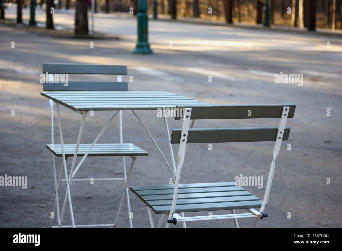 an empty cafe table with two chairs placed on a paved path in a park. Stock Photo