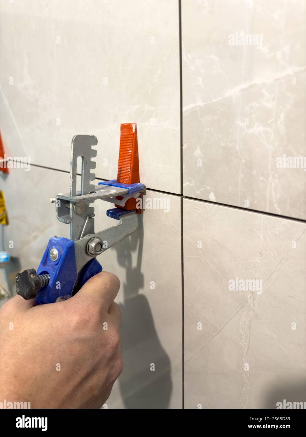 Tiling process in action with manual tile leveling tool being used Stock Photo