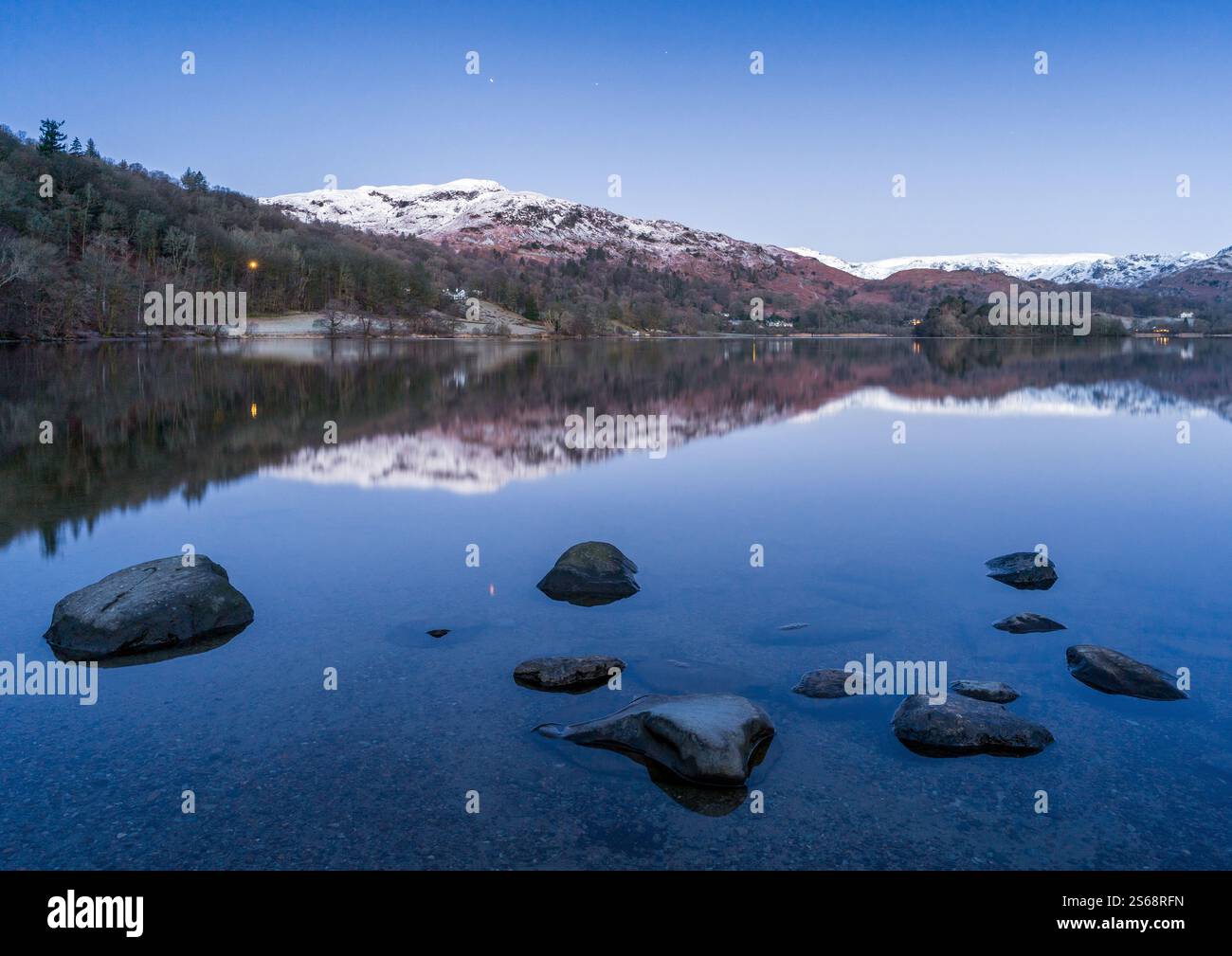 Blue hour reflections captured in Grasmere on a freezing winter morning with a completely clear, deep blue sky mirrored in the calm waters. Stock Photo