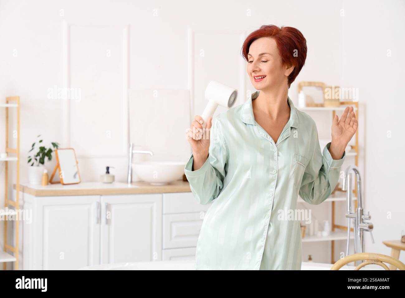 Mature redhead woman drying hair in bathroom Stock Photo - Alamy