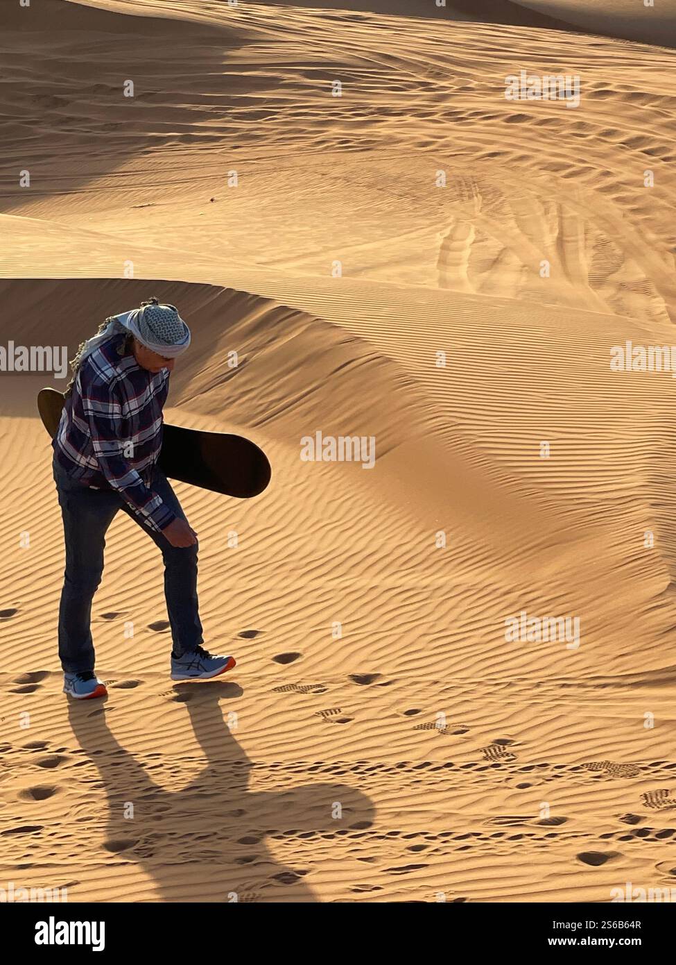 Elderly man walking with sandboard under arm up sand dune - Smartphone Captured Stock Image