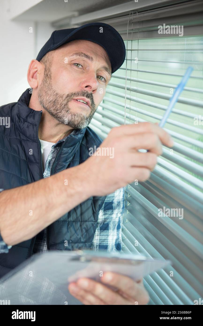 man is inspecting the window blinds Stock Photo
