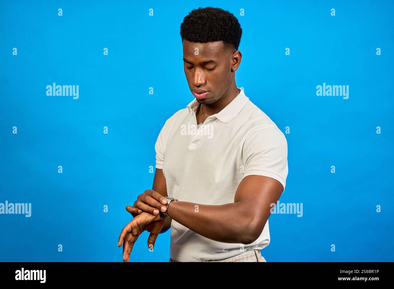 Stylish young man checking the time on his wristwatch against a vibrant ...