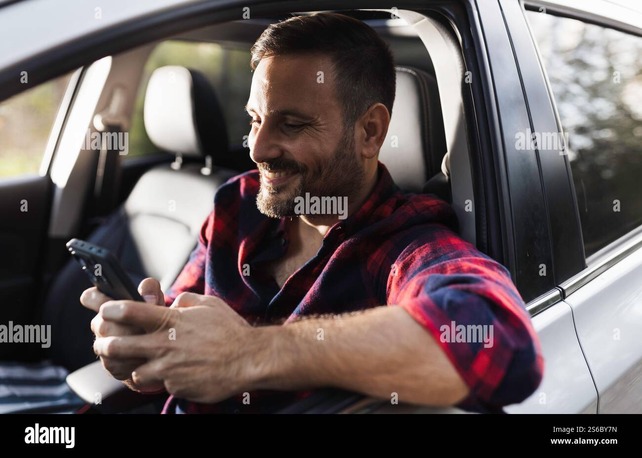 Handsome man in plaid shirt driving car and texting on mobile phone Stock Photo