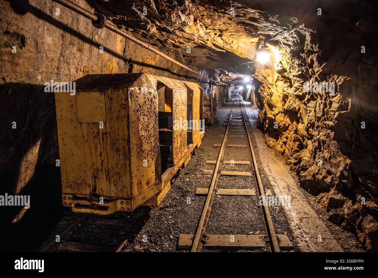 Inside the historic mine shaft of Jachymov, rusty mine carts sit on the tracks, illuminated by dim lights. The rugged walls reflect the rich mining history of the region. Stock Photo