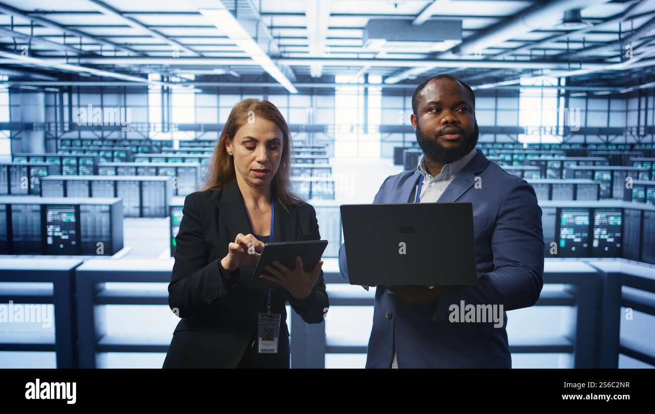Manager in data center supervising worker running error checking utilities to fix errors. Supervisor in server farm overseeing engineer repairing network issues affecting rigs performance, camera B Stock Photo