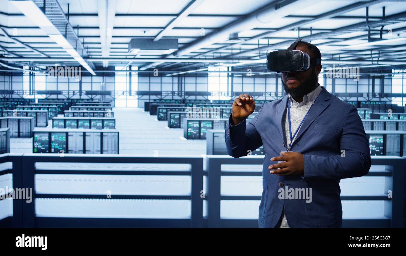 African american developer immersed in virtual reality at data center, doing units maintenance. Technician using VR headset to optimize servers performance, checking operations, camera B Stock Photo