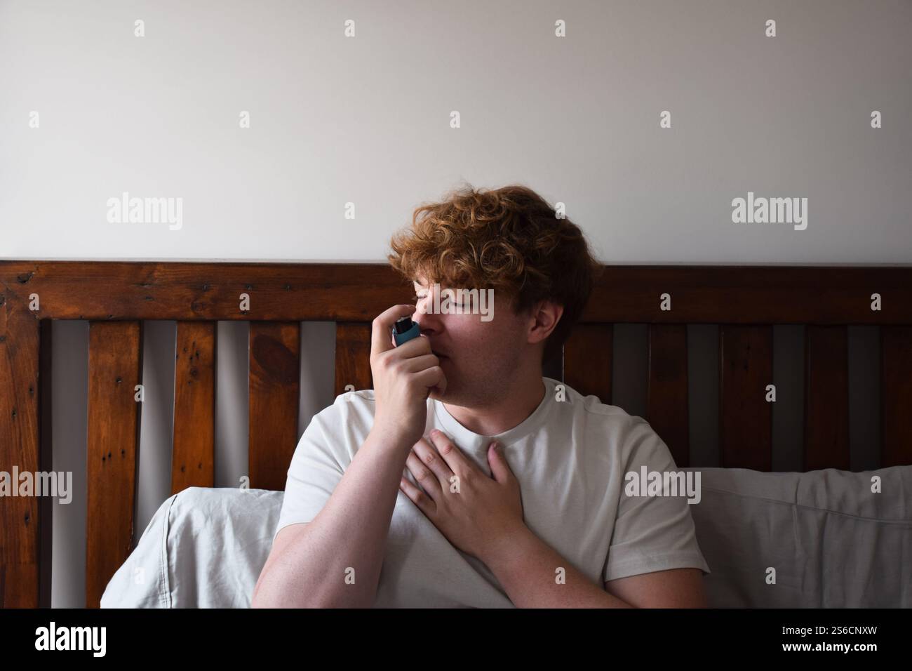 Young man sitting on bed using inhailer for asthma attack Stock Photo