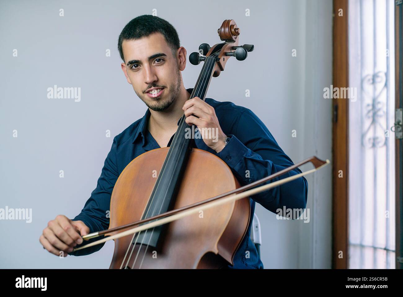 Young musician playing cello indoors with bow and strings. Stock Photo