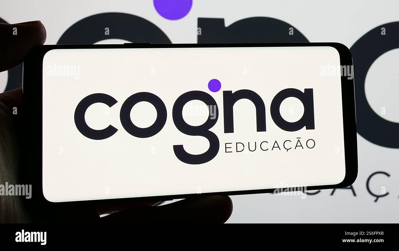 In this photo illustration, a person is holding a smartphone with the logo of Brazilian education company Cogna Educacao SA on screen. Stock Photo