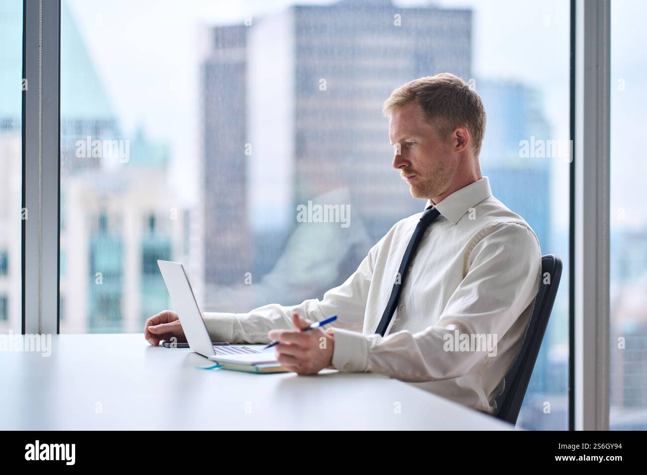 Young busy businessman looking at computer writing notes at work desk in office. Stock Photo