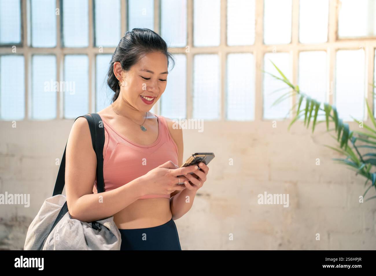 A woman dressed in stylish activewear is using her smartphone in a modern gym setting Stock Photo