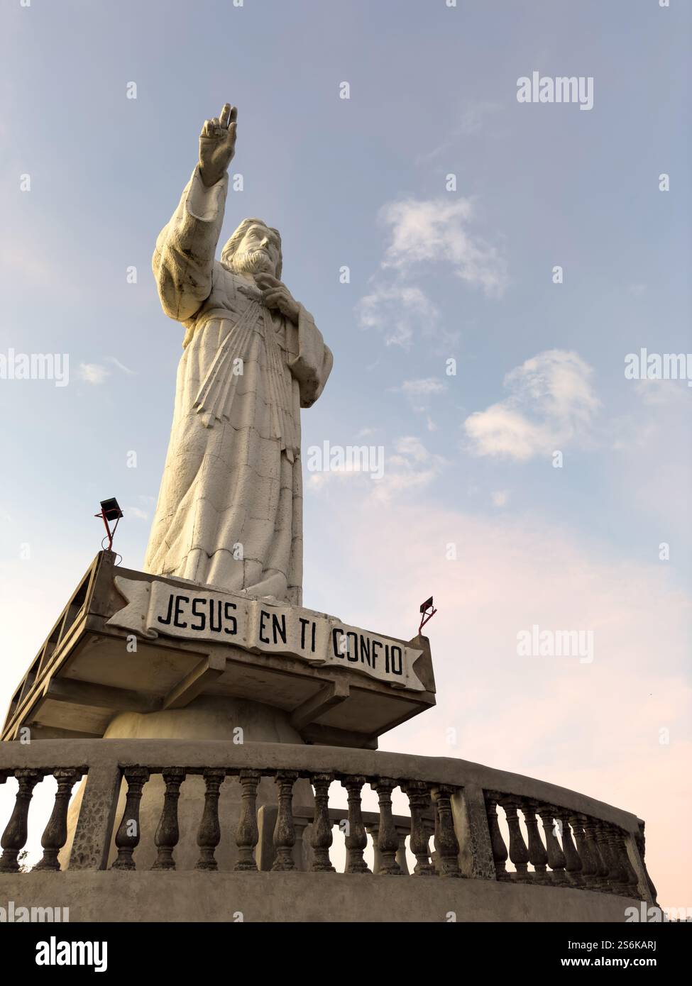 Majestic statue of Christ gestures towards sky, overlooking tranquil landscape during sunset. Stock Photo